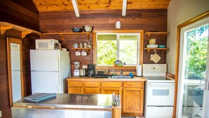 Une cuisine compacte dotée de meubles en bois, d’un réfrigérateur en acier inoxydable, d’un four à micro-ondes, d’une cuisinière et d’une fenêtre donnant sur un paysage verdoyant.