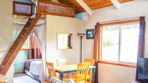 Une pièce chaleureuse avec un plafond en bois, un lit à baldaquin, une table à manger avec des chaises, un téléviseur et une fenêtre avec des rideaux.