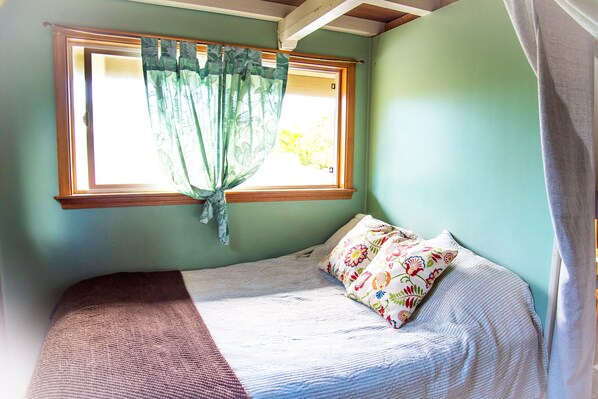 A small, single-bed room with a window, a bed with a floral pillow, and a green wall. - Bright, clean, airy Rocky Point Beach 1 bedroom loft. Steps to beach & bike path (Haleiwa)