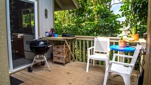 Une terrasse en bois avec un barbecue, des paniers en osier et une chaise en plastique blanche.