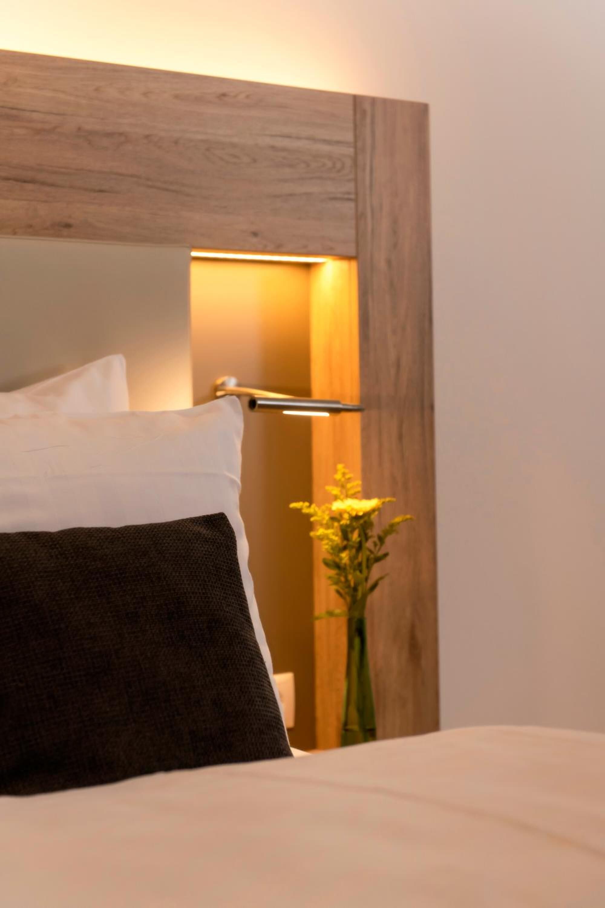 A bed with white and dark pillows, a wooden headboard, and a bedside table with a lamp.