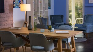 A modern living room with a wooden dining table, grey upholstered chairs, a bookshelf, and a blue sofa. - Four Stars by City Hotel (Meckenheim)