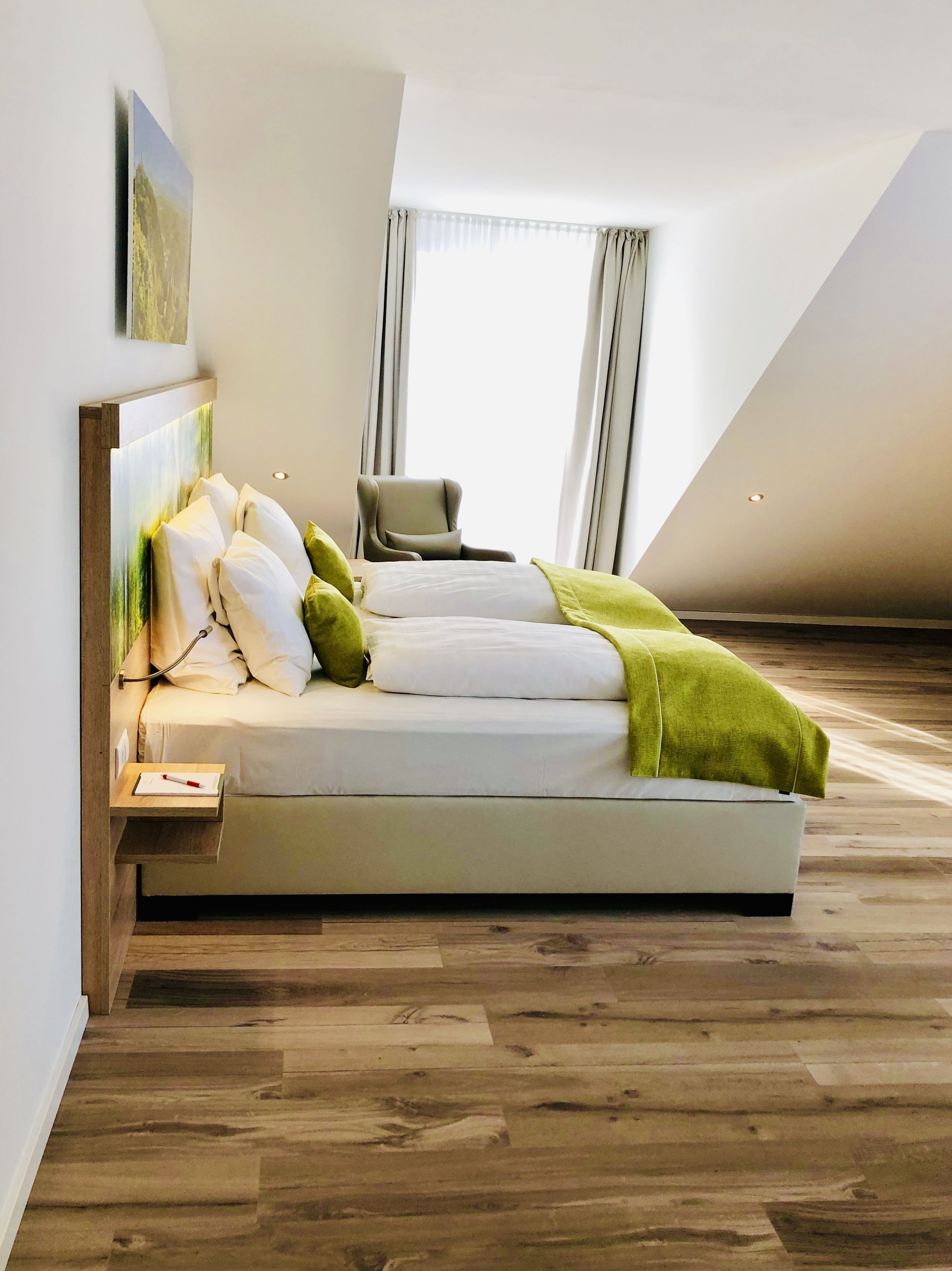 A modern bedroom with a large bed, a bedside table, a chair, and a window with curtains.
