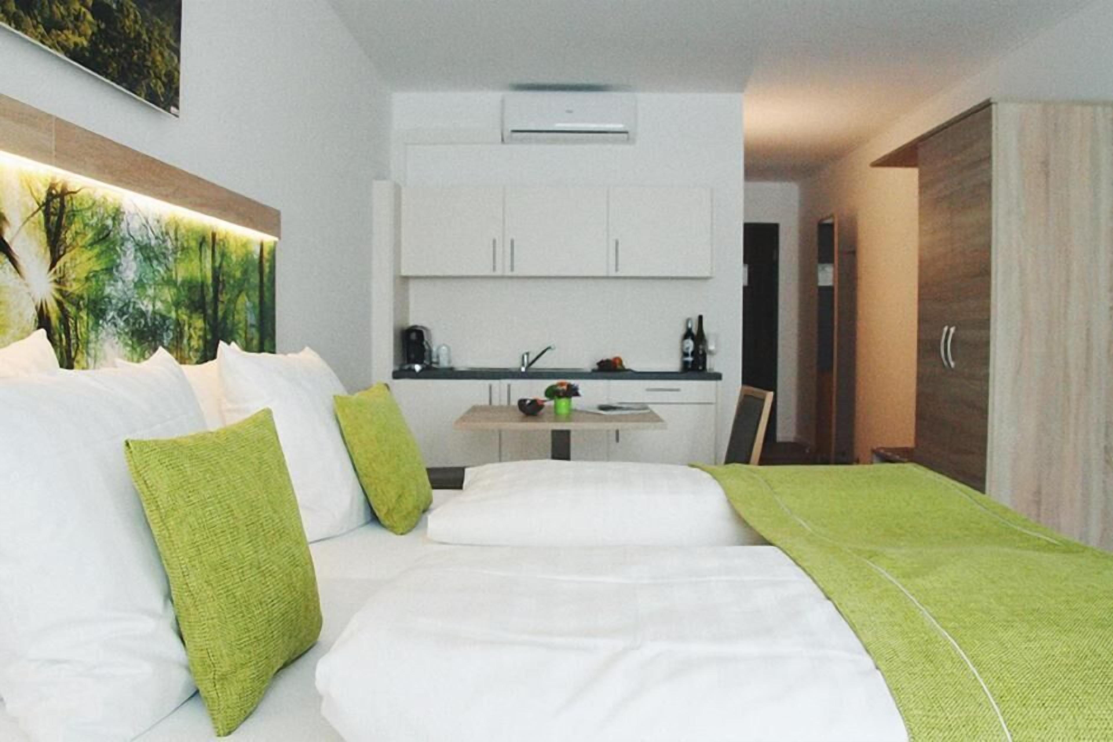 A hotel room with a bed, a small kitchenette, and a painting on the wall.