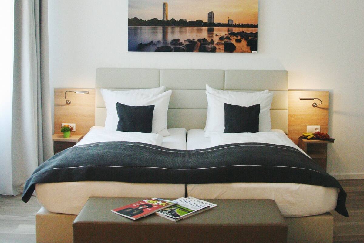 Une chambre d’hôtel avec un lit, une table de chevet, une lampe de chevet, un magazine et un tableau au mur.