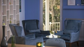A room with two blue armchairs, a small round table with a vase, a bookshelf, and a door leading to an outdoor area. - Four Stars by City Hotel (Meckenheim)