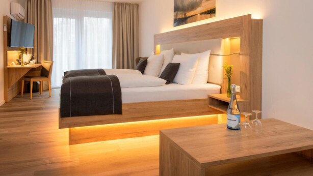 A hotel room with a bed, bedside table, and a desk with a chair. - Four Stars by City Hotel (Meckenheim)
