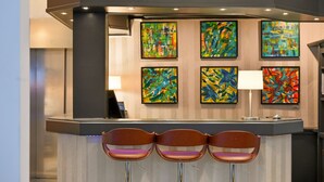 A reception area with a counter, three brown chairs, and six colorful abstract paintings on the wall. - Four Stars by City Hotel (Meckenheim)