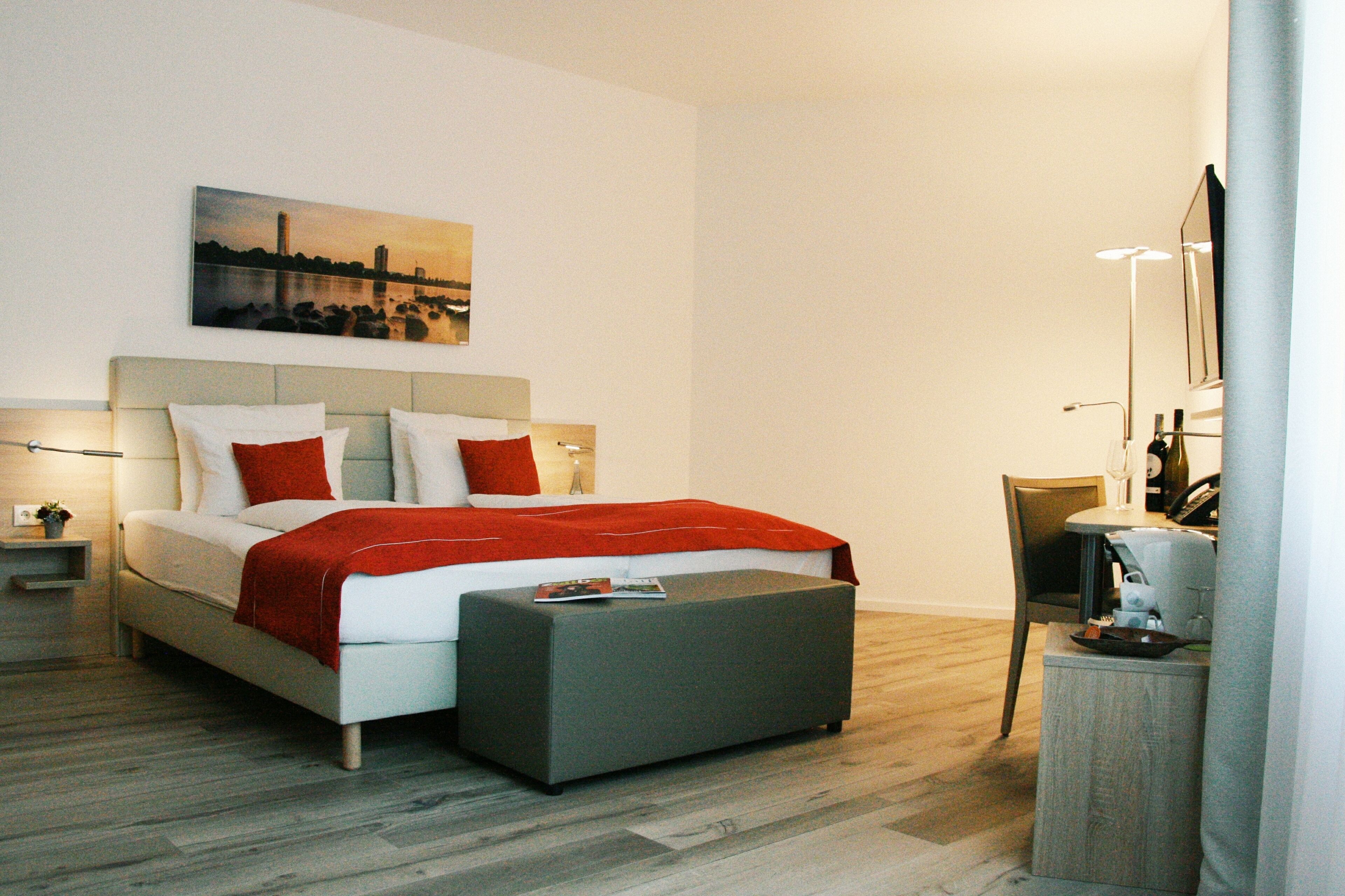 Un dormitorio moderno con cama, mesitas de noche, una silla y una pequeña mesa con lámpara.