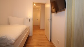 A bedroom with a bed, a television mounted on the wall, and a door leading to another room. - Wohnen am Yachthafen W45 (Cuxhaven)