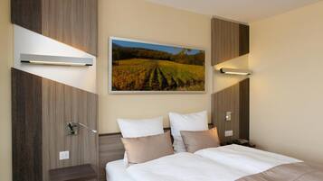 Habitación de hotel con una cama grande, dos mesitas de noche, un cuadro colgado de un viñedo e iluminación empotrada.