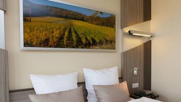 Ein Hotelzimmer mit einem großen gerahmten Bild eines Weinbergs, einem Bett mit weißen und beigen Kissen, einem Nachttisch mit Telefon und einer Wandleuchte.