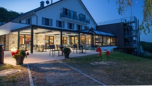 A modern two-story building with a covered patio area, outdoor seating, and a stone facade. - Hotel Restaurant Le Cleebourg (Rott)