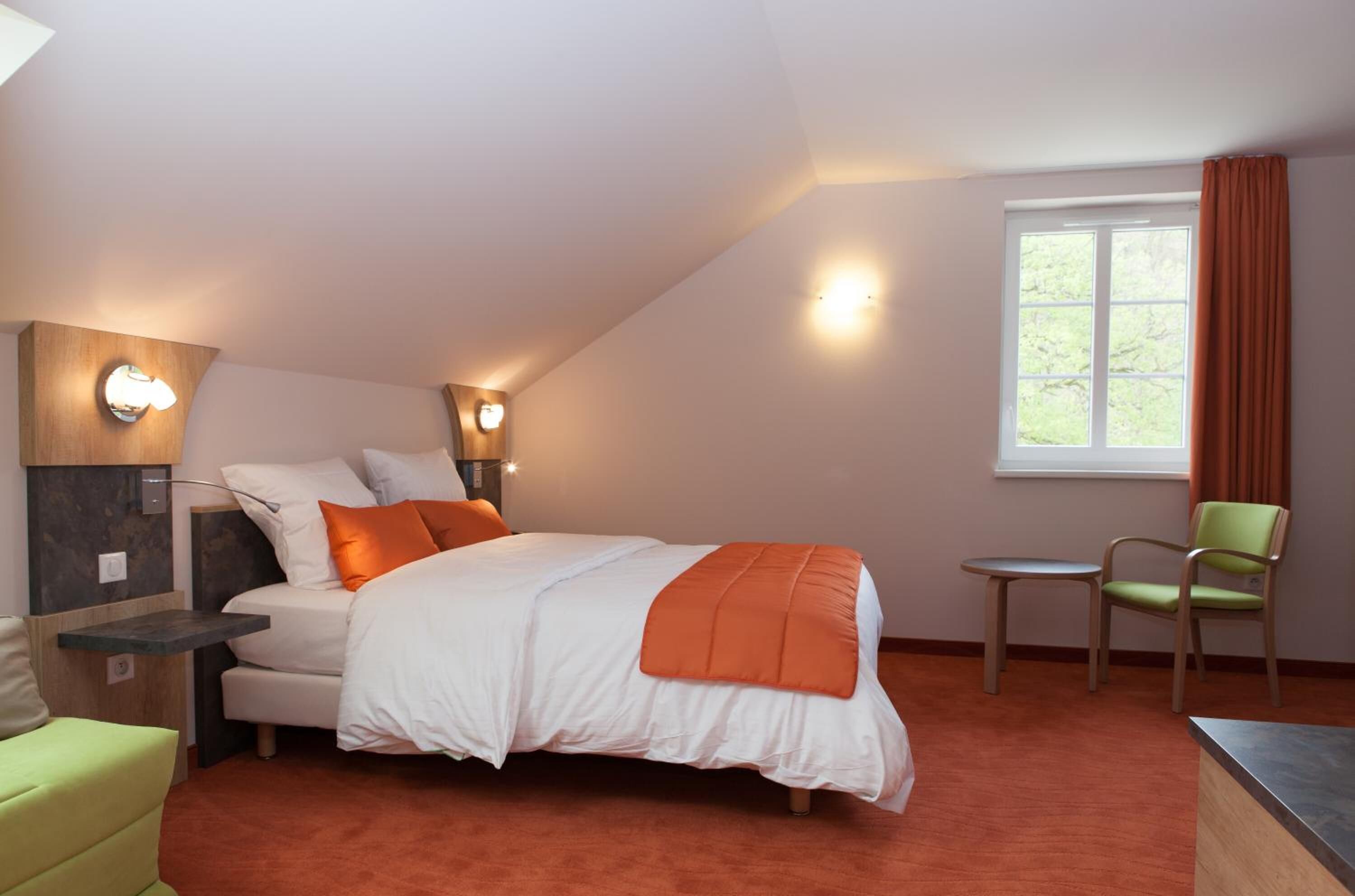 A bedroom with a bed, bedside tables, a chair, a small table, and a window with curtains.