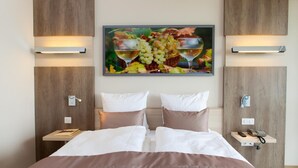 A hotel room with a bed, two bedside tables, a wall-mounted artwork of grapes and wine glasses, and wooden paneling. - Hotel Restaurant Le Cleebourg (Rott)