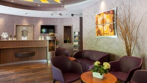A reception area with a wooden counter, purple seating, a TV, and a large abstract painting on the wall. - Hotel Restaurant Le Cleebourg (Rott)