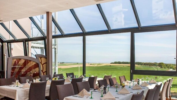 A restaurant with multiple tables set for dining, large windows offering a view of a golf course, and a modern ceiling design. - Hotel Restaurant Le Cleebourg (Rott)
