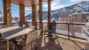 A covered patio with stone pillars, a table with chairs, and a view of snow-covered mountains and a parking area.