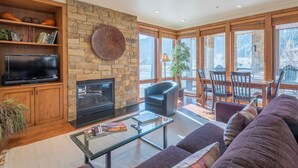 A living room with a stone fireplace, a flat-screen TV, a glass coffee table, and a sofa.