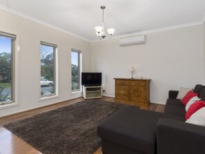 A living room with a flat-screen TV, a dark-colored sofa, a wooden cabinet, and a large window.
