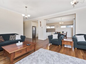 A spacious living room with a wooden coffee table, two sofas, and a rug. A kitchen is visible in the background.