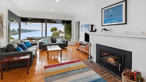 A spacious living room with a fireplace, a large window overlooking a body of water, and a modern interior design.