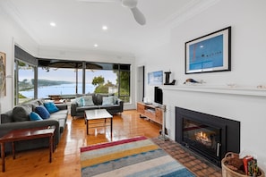 A spacious living room with a fireplace, a large window overlooking a body of water, and a modern interior design.
