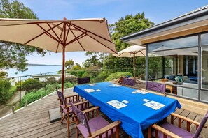 An outdoor deck with a blue tablecloth, wooden chairs, and umbrellas.