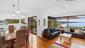 Relax in this spacious living area with a large dining table and comfortable sofa, offering a stunning view of the coastal landscape.