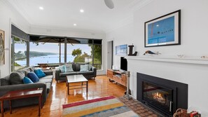 Enjoy a serene view of the water and greenery from this spacious living room with a fireplace and comfortable seating area.