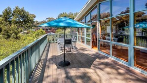 Eine Holzterrasse mit Sitzgelegenheiten und einem großen Sonnenschirm mit Blick auf eine üppige, grüne Landschaft.