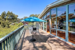 A wooden deck with outdoor seating and a large umbrella, overlooking a lush green landscape. - Wallys Place (Lorne)
