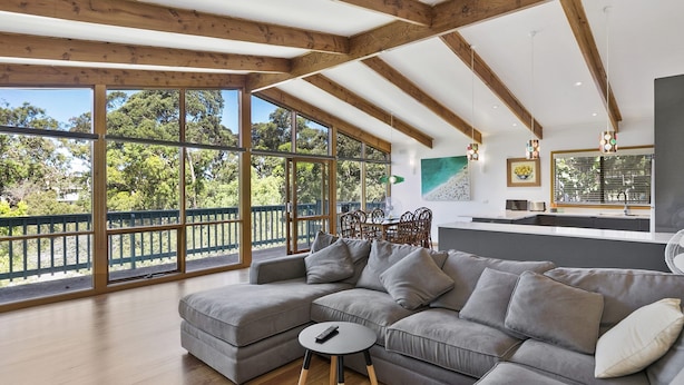 Ein modernes Wohnzimmer mit einem Ecksofa, einem kleinen runden Tisch und Blick ins Freie durch große Fenster.