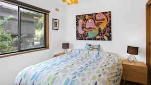Ein Schlafzimmer mit einem Bett, zwei Nachttischen, einem Fenster, einem Wandbild und einer Tür.