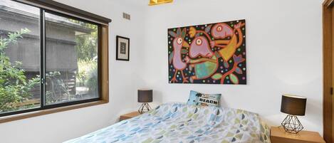 Une chambre à coucher comprenant un lit, deux tables de chevet, une fenêtre, un tableau accroché au mur et une porte.