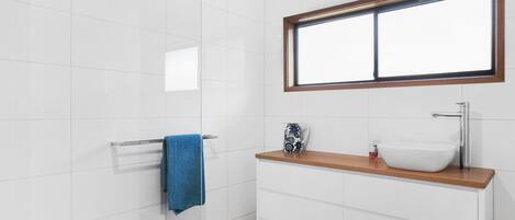 A bathroom with a white tiled wall, a wooden countertop, a white sink, a mirror above the countertop, and a blue towel hanging on a towel rack.