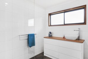 Un bany amb una paret de rajoles blanques, un taulell de fusta, un lavabo blanc, un mirall sobre el taulell i una tovallola blava penjada en un suport per a tovalloles.
