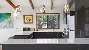 Modern kitchen with central island, sink, and oven, featuring pendant lights and a large window with horizontal blinds.