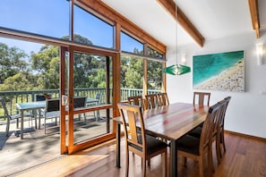 A dining area with a wooden table and chairs, large windows, and a view of the outdoors. - Wallys Place (Lorne)