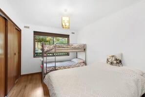 Habitació amb literes, finestra, porta de fusta i lluminària al sostre.