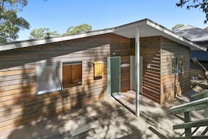A wooden cabin with a deck, a door, and a window. - Wallys Place (Lorne)