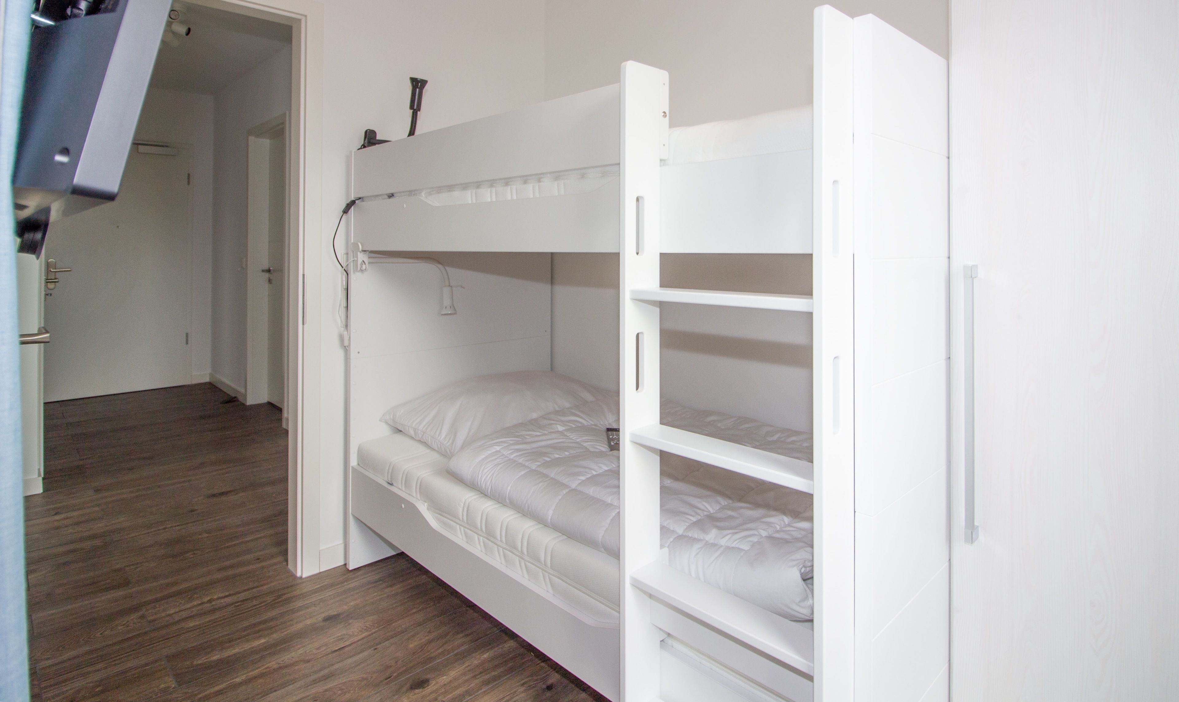 Een stapelbed met hoofdbord en een onderkast, een witte deur en een houten vloer.