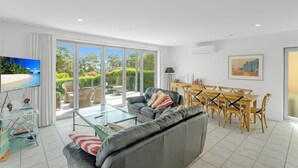 Een moderne woonkamer met een grijze bank, een glazen salontafel en een eethoek met houten stoelen en een tafel.