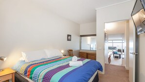 Ein Hotelzimmer mit Bett, Nachttisch, Sessel, Kommode und einem durchgegangenen Tür sichtbaren Badezimmer.