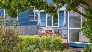 Ein blaues Haus mit Terrasse, Gartenmöbeln und verschiedenen Pflanzen.