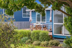 Une maison bleue avec une terrasse, du mobilier d’extérieur et diverses plantes.