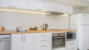 Una cocina moderna con armarios blancos, un lavamanos de acero inoxidable, un hervidor y un horno.