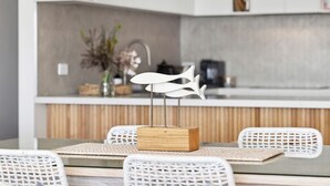 A modern kitchen with a white countertop, a wooden cabinet, and a dining area with a table and chairs. - Apartment 12 Pacific Apartments (Lorne)