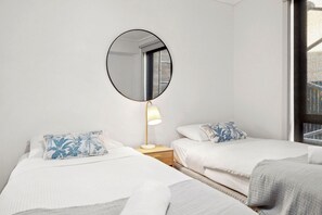 Une chambre d’hôtel avec deux lits, un miroir rond, une lampe de chevet et une fenêtre.