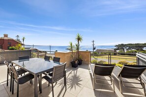 Une terrasse extérieure avec une table et des chaises, donnant sur une plage et l’océan.